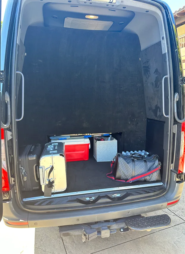 Suitcases and bags loaded in the open rear cargo area of a Mercedes-Benz Sprinter